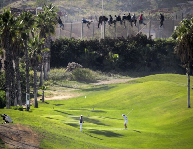 Dans l'enclave espagnole de Melilla, une joueuse de golf est concentrée sur sa séance d'entrainement face à son entraineur. Au fond, des migrants tentent de passer le grillage haut de 6 mètres, qui marque la frontière entre l'Espagne et le Maroc voisin. Certains migrants ont refusé de descendre de la grille ce jour-là malgré les ordres de la Guardia Civil (police espagnole) et sont ainsi restés suspendus près de 13 heures, en plein soleil. La photo de cette triste histoire a été publiée par le journal espagnol El Mundo à sa une et a depuis fait le tour du monde.