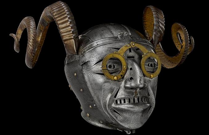 L'objet le plus reconnaissable des collections des Armures Royales est probablement le "casque à cornes" d'Henri VIII. Ce casque est remarquable par son allure grotesque, ses lunettes en laiton soutenues par un nez crochu et dégoulinant, et par ses cornes de bélier. Pendant cinq siècles, ces caractéristiques extraordinaires ont suscité les plus grands débats savants.

 Des recherches récentes suggèrent que le masque est très proche du visage du "Schellenunter", un "fou" figurant sur une carte à jouer dessinée par Peter Flötner, un artiste allemand du XVIe siècle célèbre pour ses personnages grotesques. Ce personnage a la même capuche bien ajustée, le même nez crochu et dégoulinant, le même menton poilu et les mêmes lunettes "à rivets". La présence de cornes, en revanche, reste un sujet de débat.

En 1511, deux ans après qu'Henri VIII fut devenu roi, Maximilien Ier, l'empereur du Saint Empire romain germanique, chargea son armurier, Konrad Seusenhofer, de fabriquer une armure décorée de panneaux d'argent doré comme cadeau diplomatique pour Henri. Mais de nombreux spécialistes estiment qu'il est peu probable que Maximilien ait envoyé un tel casque à Henri, les cornes étant alors souvent considérées comme le signe d'un cocu.

Source : https://collections.royalarmouries.org/object/rac-object-2623.html