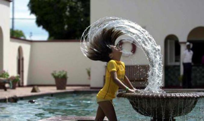 Une femme se rafraichit grâce à une fontaine.