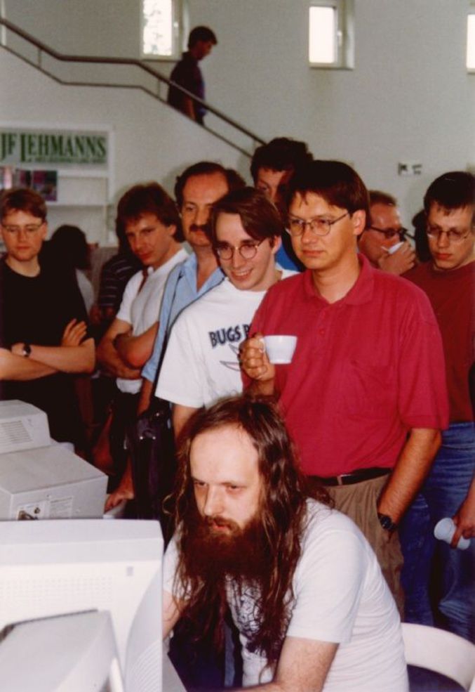 Linus Torvalds (souriant avec des lunettes en chemise blanche) observe le travail d'Alan Cox, un des principaux développeurs du noyau Linux.