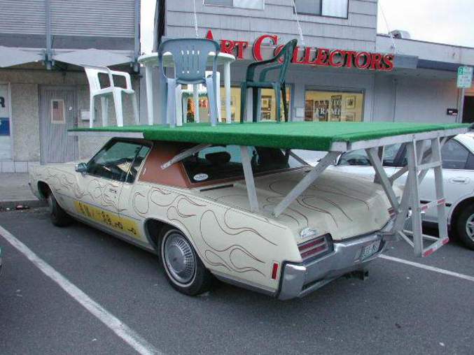 Une voiture qui transporte une table et des chaises sur son toit d'une façon plutôt inhabituelle.