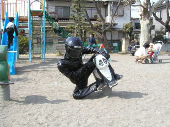 Un biker tout équipé en noir chevauche un jeu pour enfant dans une plaine de jeux