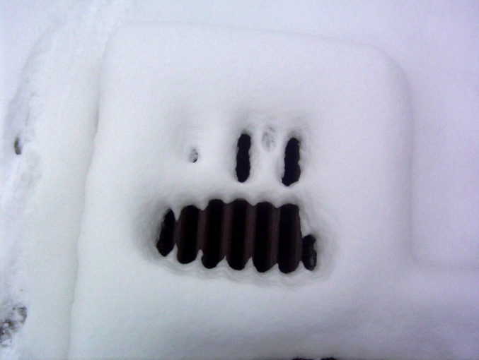 Une grille d'égoût sous la neige qui ressemble à un monstre