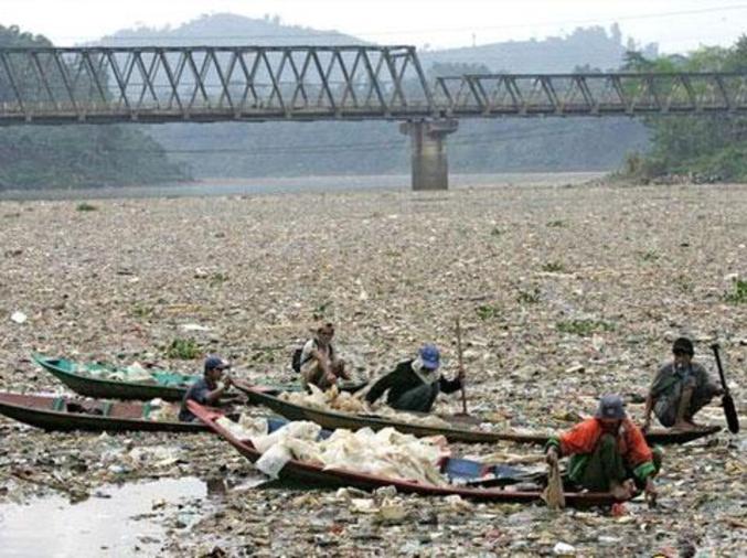 Des hommes récoltent des déchets en plastique, le long du fleuve Citarum, censé être la ressource principale en eau douce et potable de l'Ile de Java (Indonésie).