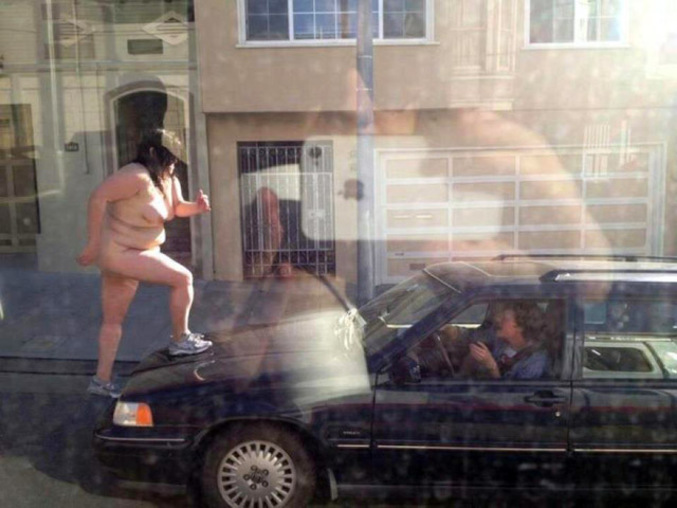 Une femme nue attaque une voiture dans la rue.