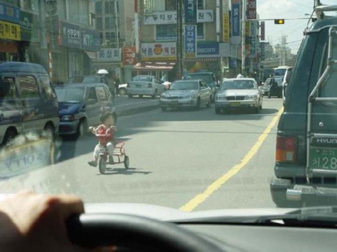 Un enfant fait du tricycle sur une route encombrée.