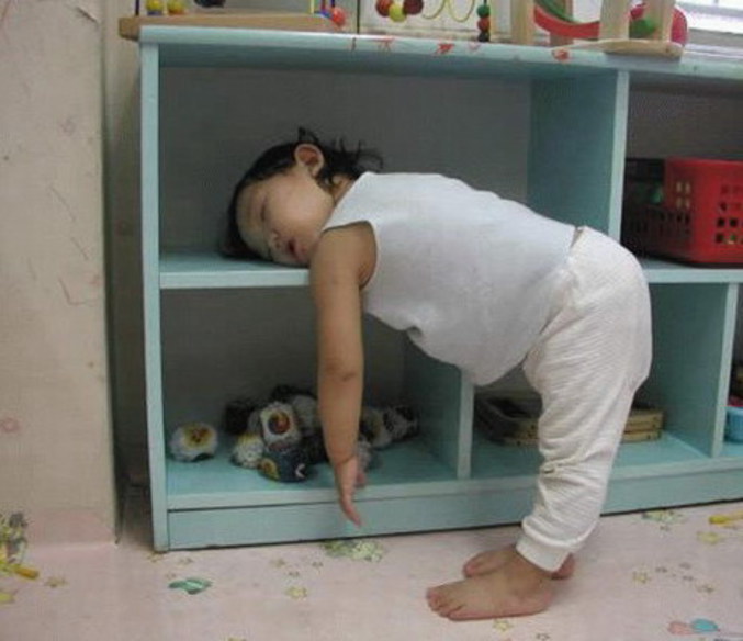 Un bébé qui dort debout la tête sur une étagère.