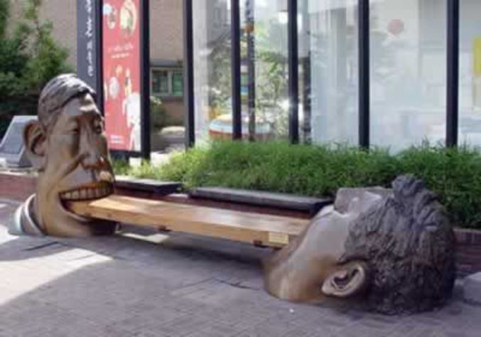 2 statues semblent dévorer un banc.