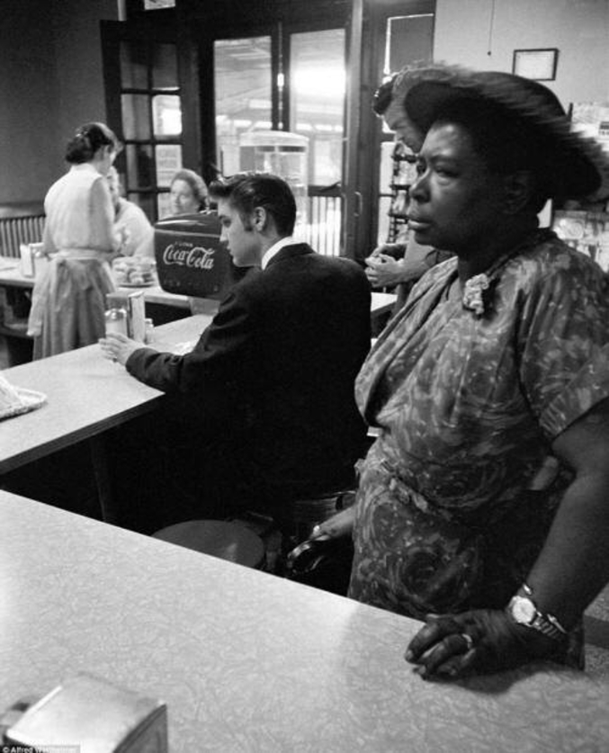 Pas toujours une question de choix. Elvis Presley boit une consommation dans un bar, tandis qu'une femme noire doit attendre sa commande debout, du fait de la ségrégation. Etats-Unis, 1966.