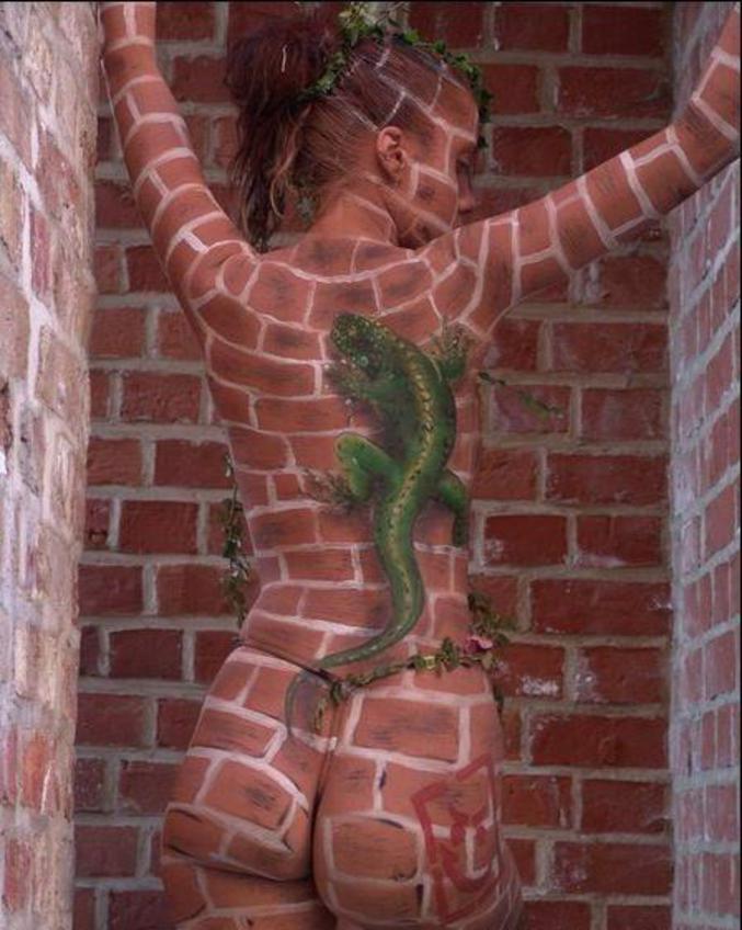 Une peinture sur le corps d'une fille nue, qui représente un caméléon sur des briques