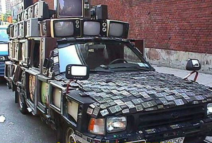 Une voiture entièrement recouverte de télés et de télécommandes.